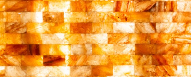 Close-up of a wall made of rectangular orange and yellow salt stone tiles with a glossy finish, arranged in a horizontal brick pattern.